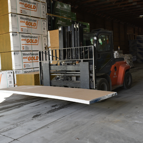 A forklift with plywood panels stacked on the forks.